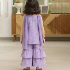 Child wearing a purple outfit with floral patterns in a room with wooden furniture.