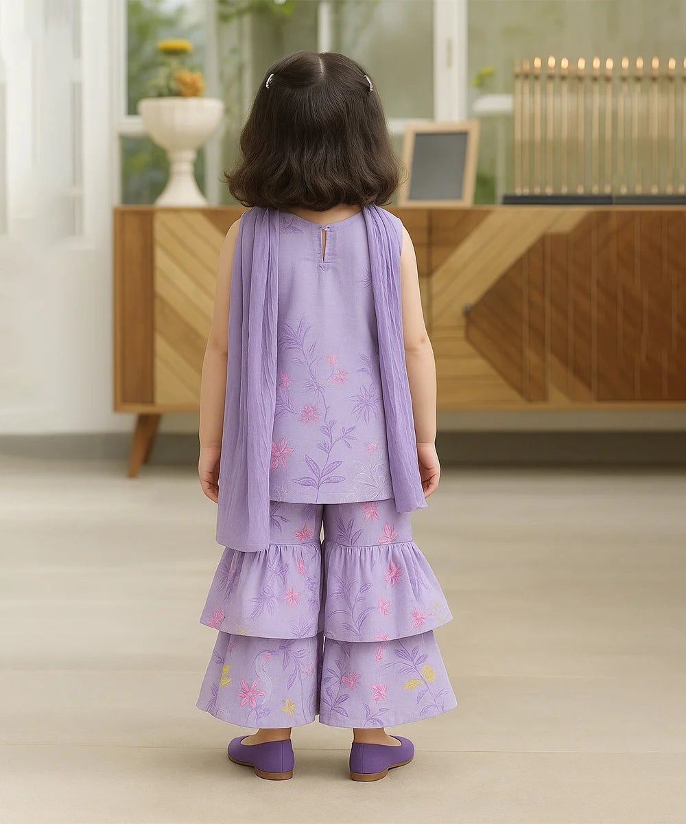 Child wearing a purple outfit with floral patterns in a room with wooden furniture.