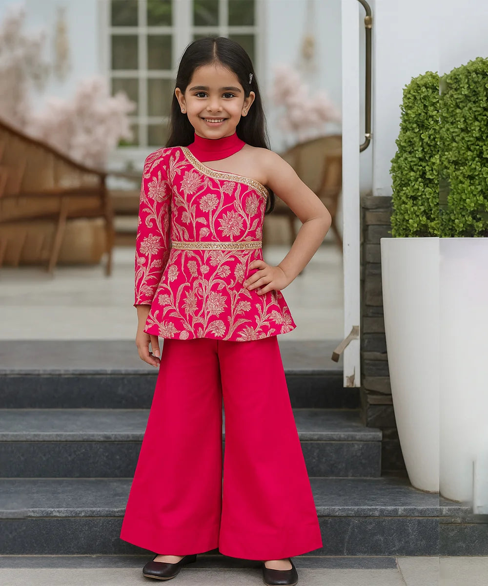 Young girl in a pink traditional outfit standing on steps outdoors.