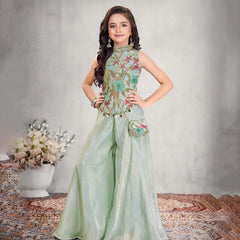 Young girl in a floral top and light green pants posing against a neutral background.