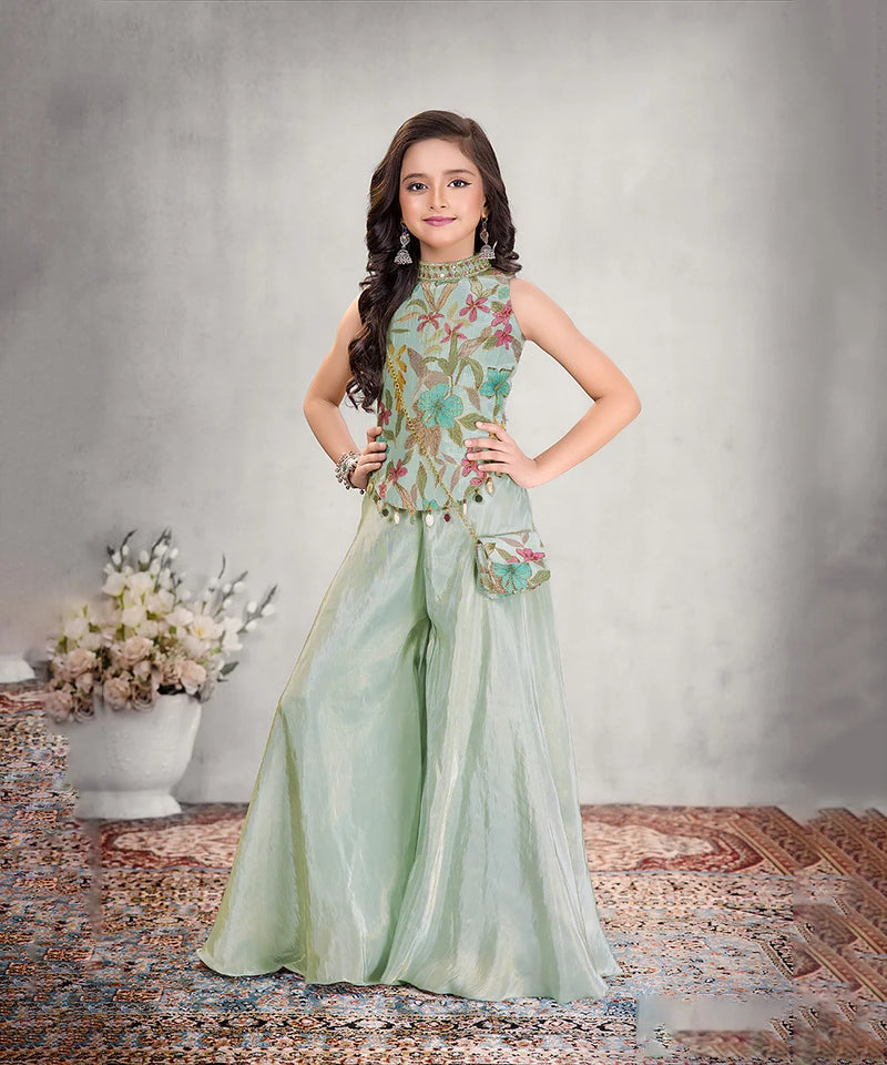 Young girl in a floral top and light green pants posing against a neutral background.