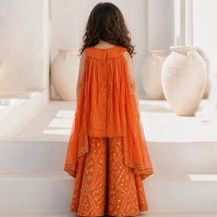 Person wearing an orange traditional outfit standing on a white staircase with decorative vases in the background.