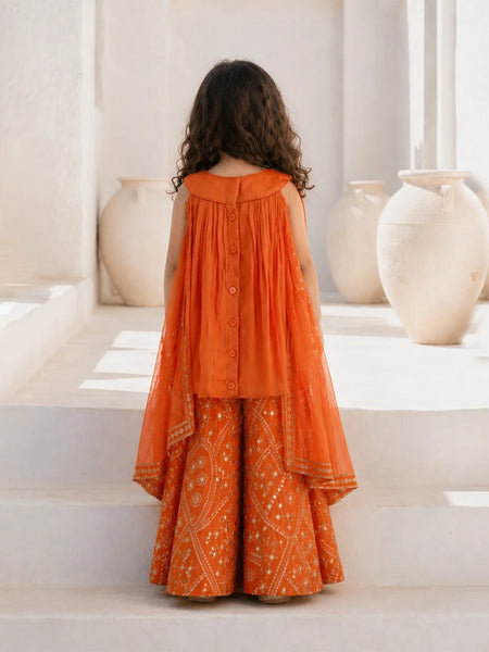 Person wearing an orange traditional outfit standing on a white staircase with decorative vases in the background.