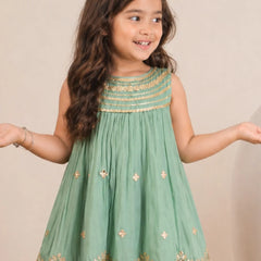 Young girl wearing a green dress with gold embroidery against a beige background
