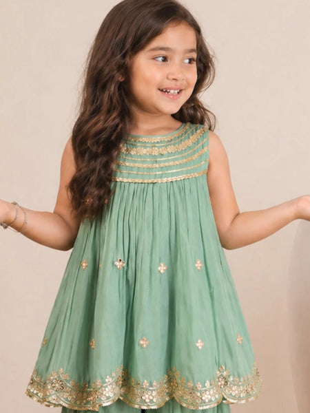 Young girl wearing a green dress with gold embroidery against a beige background