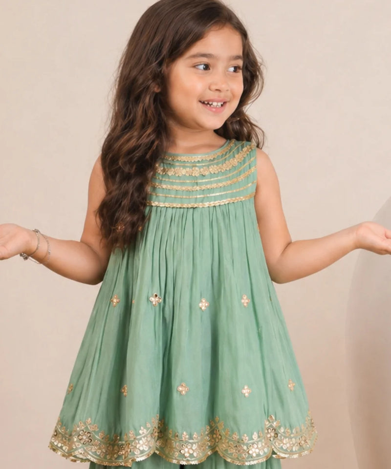 Young girl wearing a green dress with gold embroidery against a beige background