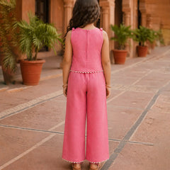 Child wearing a pink outfit standing in an outdoor setting with plants and stone pavement.