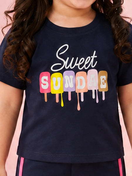 A child wearing a navy blue t-shirt with a colorful graphic that reads 'Sweet SUNDAE' in dripping popsicle shapes, set against a solid pink background.