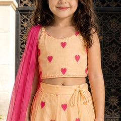 Young girl wearing a peach outfit with pink heart patterns and a pink dupatta.