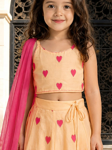 Young girl wearing a peach outfit with pink heart patterns and a pink dupatta.
