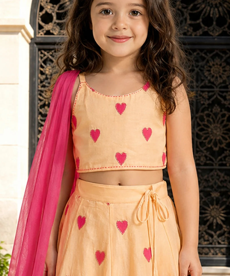 Young girl wearing a peach outfit with pink heart patterns and a pink dupatta.
