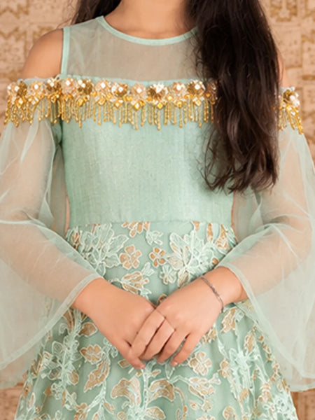 A woman wearing a mint green off-the-shoulder dress with sheer long sleeves, gold beaded fringe across the neckline, and a matching embroidered skirt.