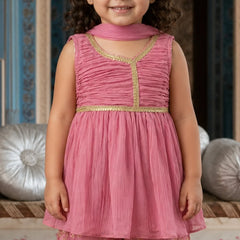 Young girl wearing a pink traditional outfit with gold details, standing against a decorative background.