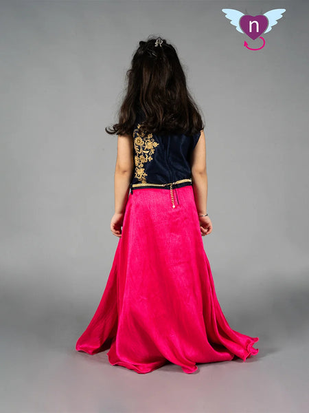 Person wearing a black top with gold embroidery and a pink skirt on a gray background