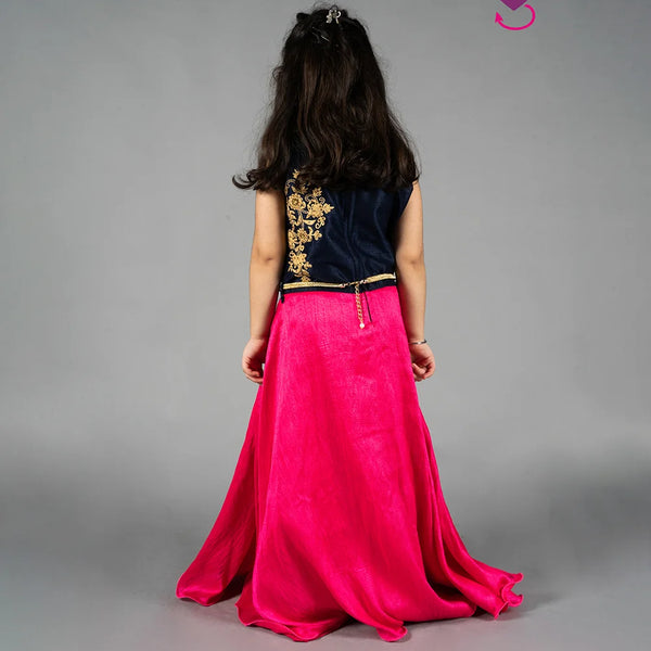 Person wearing a black top with gold embroidery and a pink skirt on a gray background