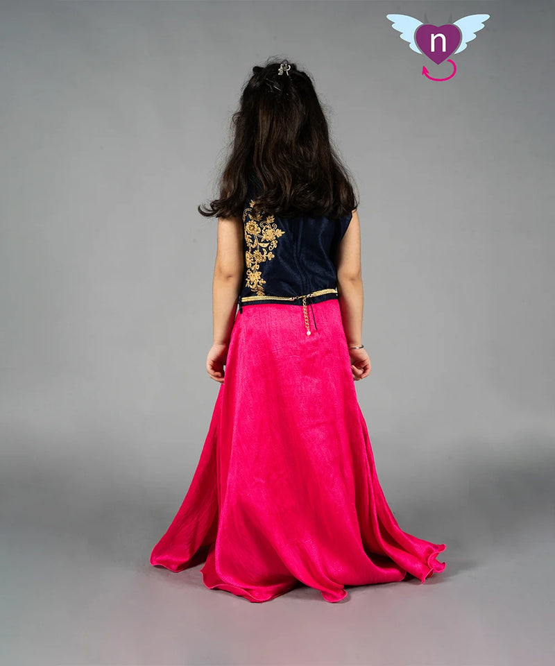 Person wearing a black top with gold embroidery and a pink skirt on a gray background