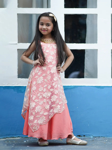 Young girl in a pink floral dress standing against a white and blue wall.