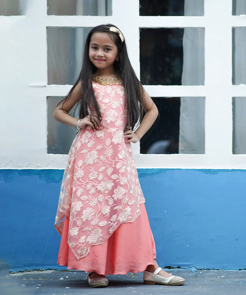 Young girl in a pink floral dress standing against a white and blue wall.