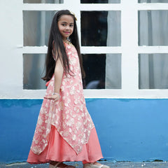 Young girl in a pink floral dress standing in front of a white window frame with blue wall.