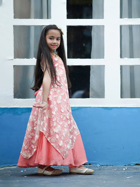 Young girl in a pink floral dress standing in front of a white window frame with blue wall.