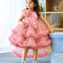 A young girl wearing a pink tiered tulle party dress with a sequined bodice and ruffled layers, standing indoors next to a blue-and-white striped basket.