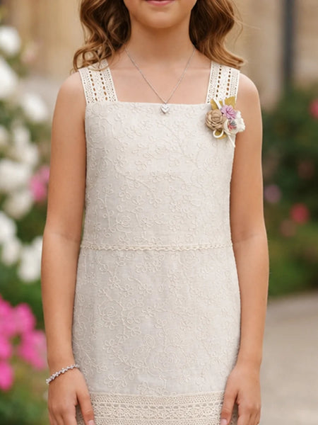 A sleeveless cream lace dress with decorative shoulder straps and a floral embellishment on the chest, worn by a young girl in an outdoor garden setting.