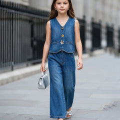 A young girl walking on a city sidewalk wearing a sleeveless blue denim vest and matching wide-leg denim pants, holding a small silver handbag.