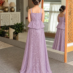 A young girl viewed from behind wearing a lavender purple sequined formal gown with a peplum waist, standing in a decorated indoor hallway with a mirror reflecting her profile.