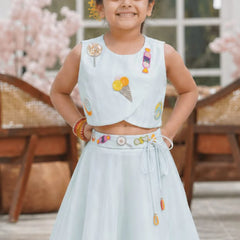 Young girl in a light blue traditional outfit with colorful embroidery, standing outdoors.