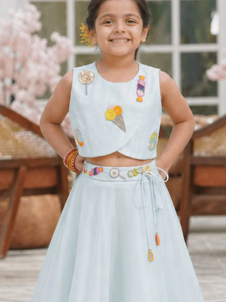 Young girl in a light blue traditional outfit with colorful embroidery, standing outdoors.