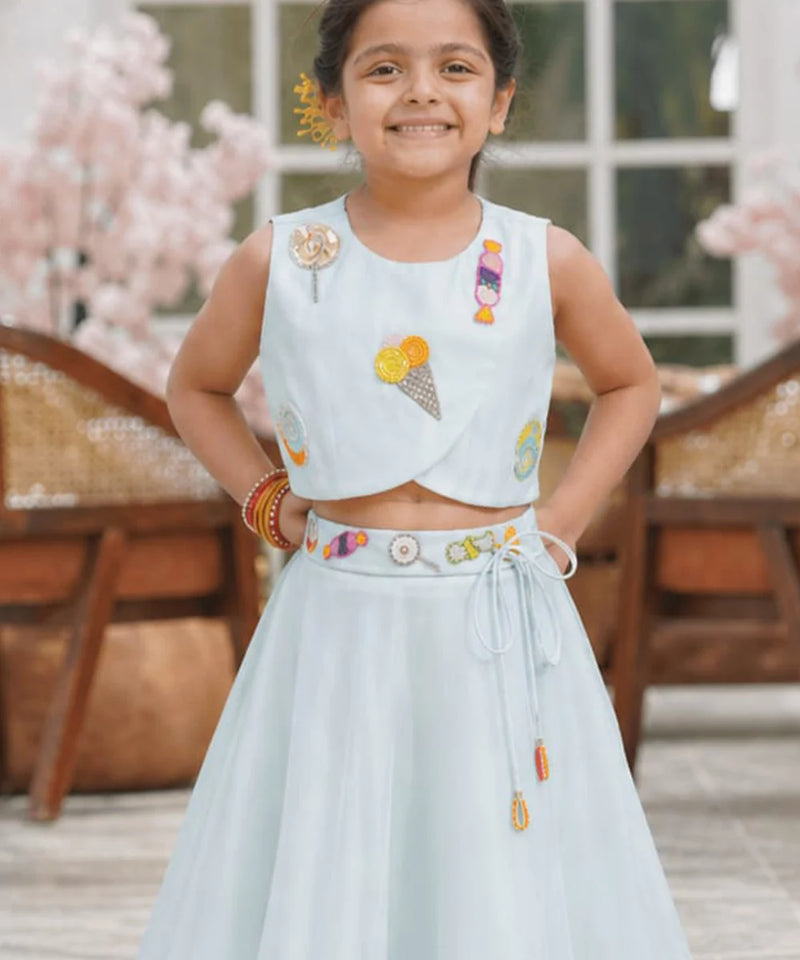 Young girl in a light blue traditional outfit with colorful embroidery, standing outdoors.