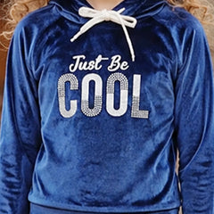 A close-up of a person wearing a royal blue velvet hoodie with a white drawstring and a rhinestone-style graphic that reads 'Just Be COOL' across the chest.