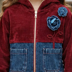 A close-up of a child wearing a zip-up hooded jacket made from a burgundy velvet fabric and blue denim. The jacket features two large blue fabric flowers on the chest, a gold zipper, and two front patch pockets.
