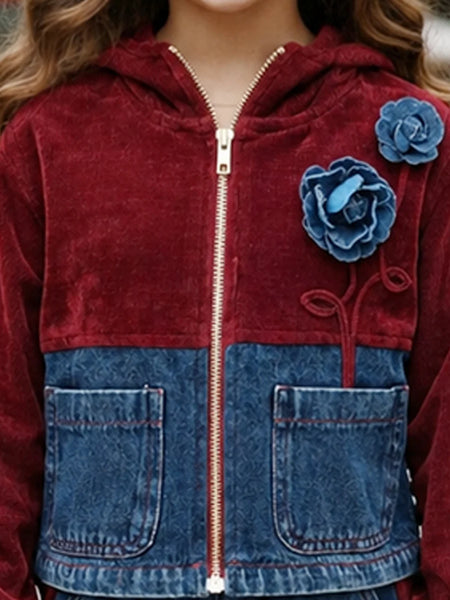 A close-up of a child wearing a zip-up hooded jacket made from a burgundy velvet fabric and blue denim. The jacket features two large blue fabric flowers on the chest, a gold zipper, and two front patch pockets.