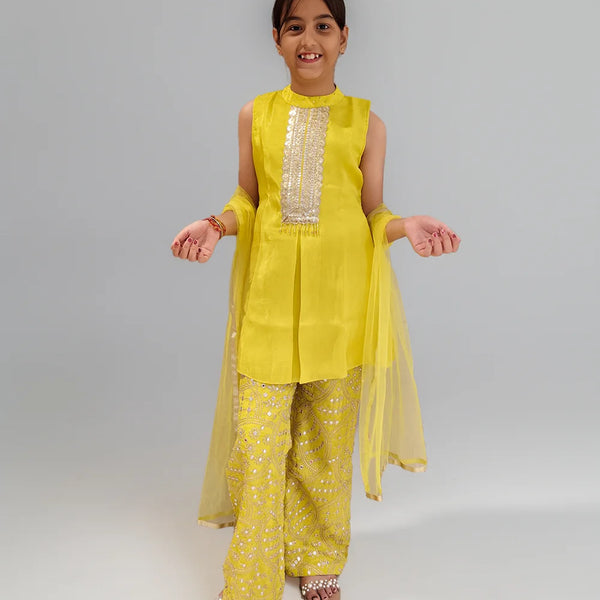 Young girl wearing a yellow sharara  traditional outfit with a plain background