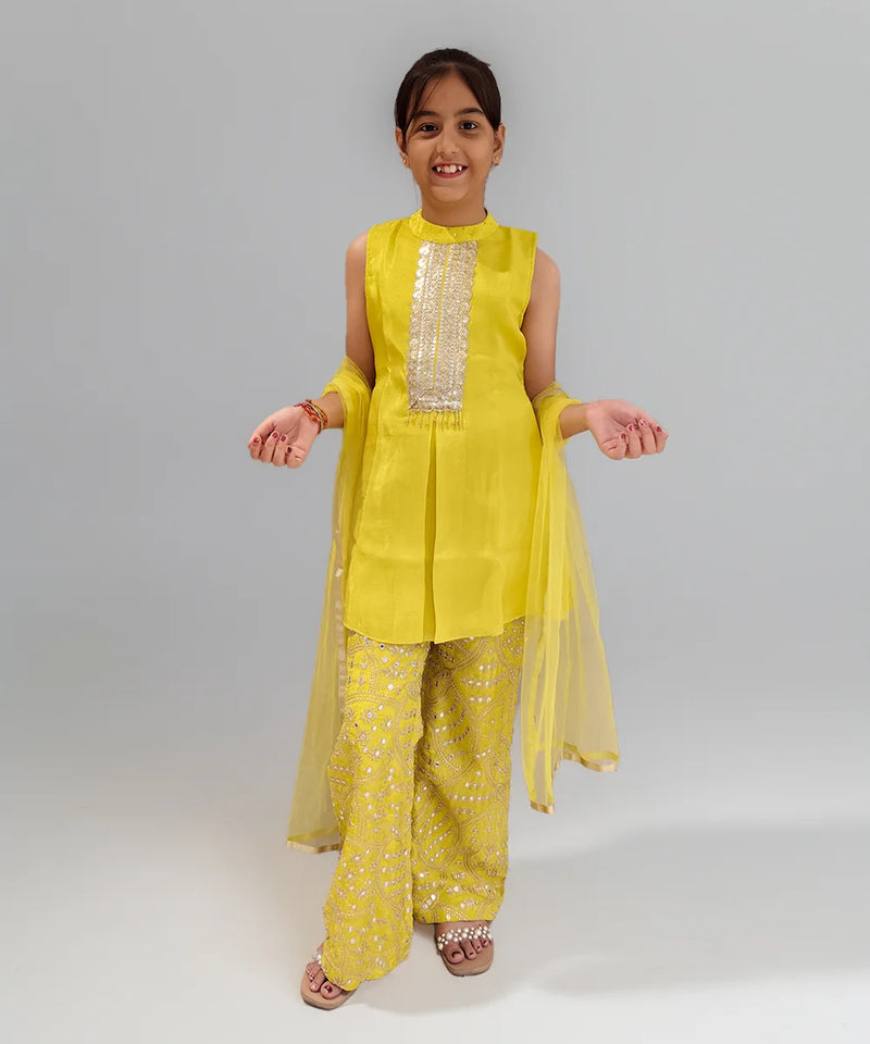 Young girl wearing a yellow sharara  traditional outfit with a plain background