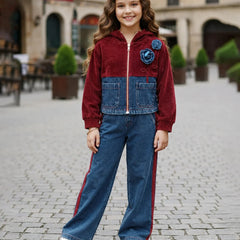 A young girl stands in a cobblestone outdoor plaza wearing a two-tone zip-up jacket made of burgundy velvet and blue denim, paired with wide-leg blue jeans featuring red side stripes and white sneakers.