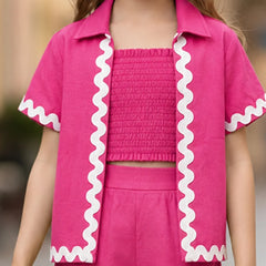 A child wearing a bright pink matching outfit with a short-sleeve collared shirt featuring white wavy trim, a smocked crop top, and matching shorts.