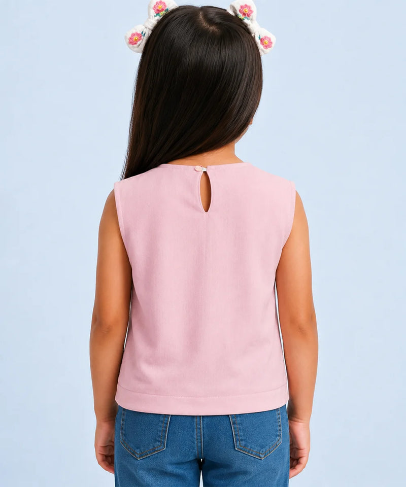 A child model shown from the back wearing a sleeveless light pink top with a small keyhole cutout at the neckline, paired with blue jeans against a light blue background.