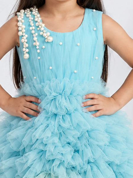 A young girl wearing a light blue tulle dress with pearl bead embellishments on the bodice and shoulder straps, posed against a light gray background.