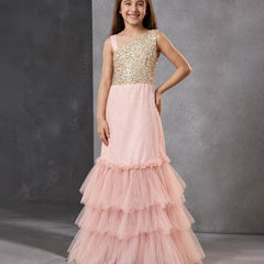 A young girl models a formal one-shoulder mermaid gown with a gold sequined bodice and a layered pink tulle skirt, set against a textured gray studio backdrop.