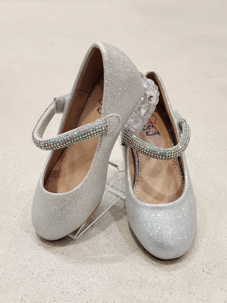 Pair of silver glitter shoes with rhinestone straps on a beige background