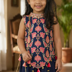 Young girl wearing a traditional embroidered top with pink floral patterns and red tassels.