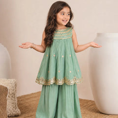 Young girl in a green dress with gold details standing on a beige carpet.