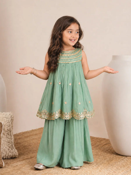 Young girl in a green dress with gold details standing on a beige carpet.
