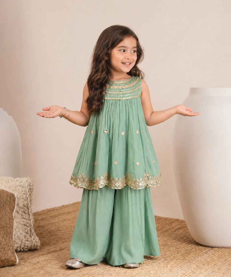 Young girl in a green dress with gold details standing on a beige carpet.