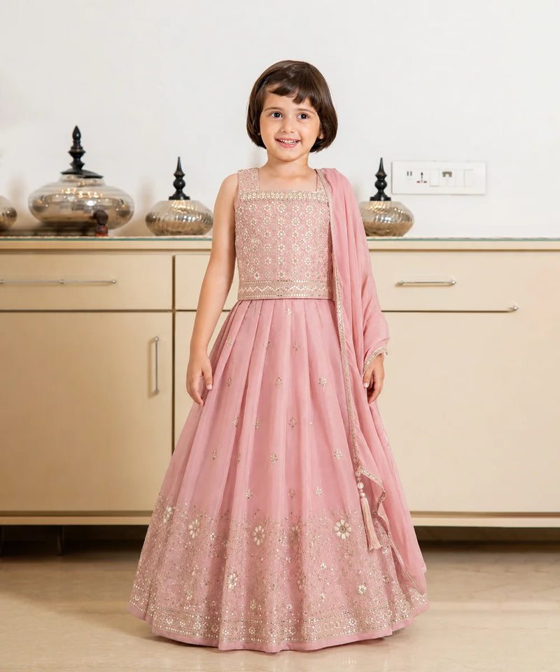 Young girl in a pink traditional outfit standing in a kitchen.