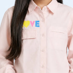 A close-up of a model wearing a light pink button-down shirt with a colorful 'LOVE' graphic on the chest, featuring a yellow heart and blue and pink letters.