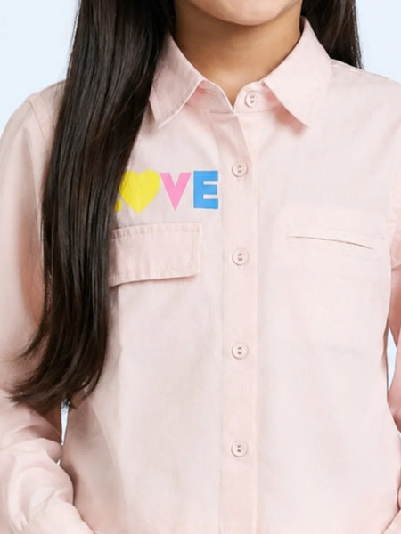 A close-up of a model wearing a light pink button-down shirt with a colorful 'LOVE' graphic on the chest, featuring a yellow heart and blue and pink letters.