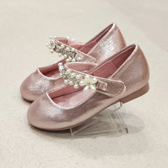 Pair of pink glittery shoes with embellishments on a light background